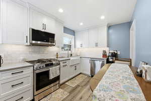 Kitchen with stainless steel appliances, white cabinets, light wood-type flooring, recessed lighting, and light stone countertops