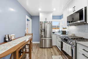 Kitchen featuring stainless steel appliances, white cabinets, light wood finished floors, light stone countertops, and decorative backsplash