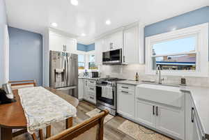 Kitchen featuring appliances with stainless steel finishes, white cabinets, light wood finished floors, light stone counters, and backsplash