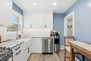 Kitchen featuring white cabinets, stainless steel appliances, light wood-style floors, backsplash, and light stone counters