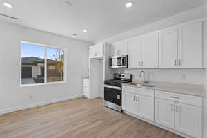 Kitchen with stainless steel appliances, white cabinetry, light wood-style floors, and recessed lighting