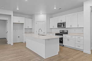 Kitchen featuring appliances with stainless steel finishes, white cabinetry, an island with sink, light wood finished floors, and recessed lighting