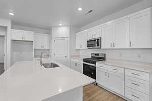 Kitchen with stainless steel appliances, white cabinets, a kitchen island with sink, light stone countertops, and recessed lighting