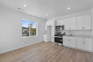 Kitchen with appliances with stainless steel finishes, white cabinetry, light wood-style floors, and recessed lighting