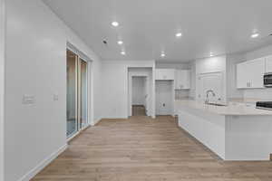 Kitchen with white cabinets, light wood-style flooring, recessed lighting, a center island with sink, and light stone counters