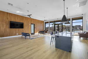 Living room featuring wooden walls, ceiling fan, light wood finished floors, and a wall of windows
