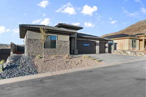 Prairie-style house with driveway, stucco siding, an attached garage, stone siding, and a mountain view