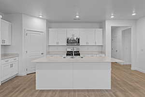 Kitchen featuring white cabinetry, appliances with stainless steel finishes, a center island with sink, light wood finished floors, and recessed lighting