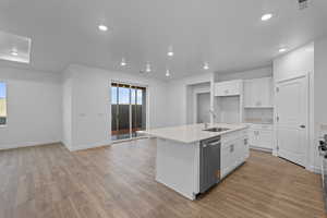 Kitchen featuring white cabinets, light wood-type flooring, an island with sink, light stone countertops, and recessed lighting