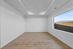 Empty room with light wood-style flooring, a raised ceiling, recessed lighting, and a mountain view