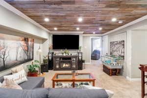 Living area with carpet floors, a glass covered fireplace, ornamental molding, and wood ceiling