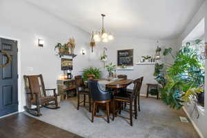 Carpeted dining space featuring lofted ceiling and a chandelier