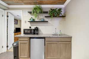 Indoor wet bar with light brown cabinetry, open shelves, crown molding, and light stone counters