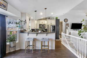 Kitchen with cream cabinets, dark countertops, pendant lighting, a peninsula, and a kitchen breakfast bar