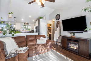 Living room featuring wood tiled floors, vaulted ceiling, ceiling fan, a glass covered fireplace, and recessed lighting