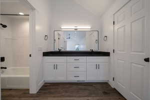 Full bath featuring lofted ceiling, double vanity, dark wood-style flooring, and shower / bath combination