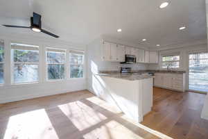 Kitchen featuring white cabinetry, a peninsula, light wood-type flooring, light stone counters, and stainless steel appliances
