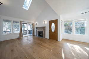 Unfurnished living room featuring plenty of natural light, a skylight, light wood finished floors, high vaulted ceiling, and a tiled fireplace