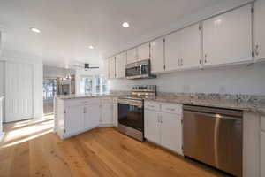 Kitchen featuring appliances with stainless steel finishes, a peninsula, white cabinetry, light wood-type flooring, and recessed lighting