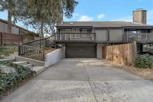 Rear view of house featuring a chimney, a deck, a shingled roof, and concrete driveway