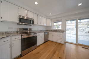 Kitchen with stainless steel appliances, white cabinets, light wood-type flooring, light stone counters, and recessed lighting