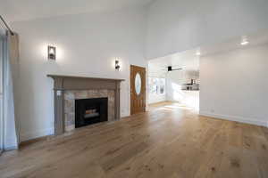 Unfurnished living room featuring high vaulted ceiling, light wood-style floors, a tile fireplace, and ceiling fan