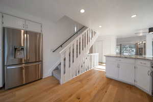 Kitchen featuring stainless steel refrigerator with ice dispenser, white cabinets, light stone countertops, light wood finished floors, and recessed lighting
