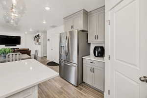 Kitchen featuring gray cabinetry, light wood-style floors, stainless steel refrigerator with ice dispenser, open floor plan, and recessed lighting