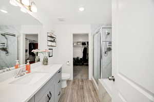 Bathroom featuring a walk in closet, vanity, a marble finish shower, and light wood-style floors