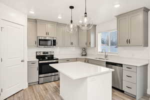 Kitchen featuring appliances with stainless steel finishes, pendant lighting, a kitchen island, gray cabinets, and tasteful backsplash
