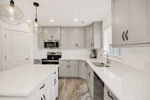 Kitchen with appliances with stainless steel finishes, hanging light fixtures, light wood-style flooring, light stone countertops, and a center island