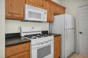 Kitchen with white appliances, dark countertops, and light tile patterned floors