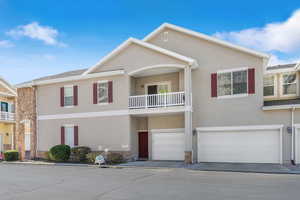 View of front of home with stucco siding, a balcony, and an attached garage