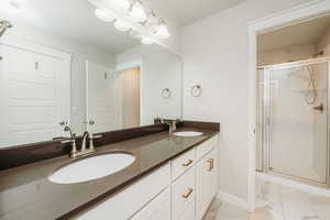 Full bath featuring double vanity, light marble finish flooring, and a stall shower