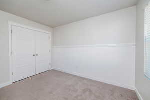 Unfurnished bedroom featuring carpet, a closet, and wainscoting