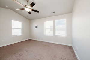 Carpeted spare room featuring lofted ceiling, plenty of natural light, and a ceiling fan