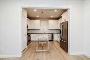 Kitchen with white cabinetry, appliances with stainless steel finishes, light wood-style flooring, decorative backsplash, and recessed lighting
