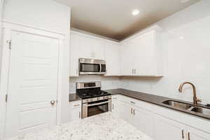 Kitchen with stainless steel appliances, white cabinetry, decorative backsplash, dark stone countertops, and recessed lighting