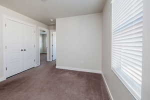 Unfurnished bedroom with dark carpet, multiple windows, a closet, and a textured ceiling