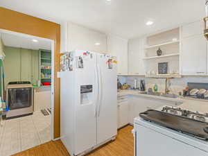 Kitchen with white appliances, open shelves, light countertops, white cabinets, and washer / dryer