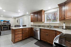 Kitchen featuring a peninsula, electric range, a glass covered fireplace, a textured ceiling, and plenty of natural light