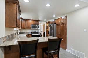 Kitchen with light stone countertops, stainless steel appliances, a kitchen bar, recessed lighting, and a peninsula