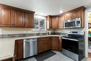Kitchen featuring stainless steel appliances, light tile patterned floors, light stone counters, a textured ceiling, and recessed lighting