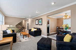 Living area featuring ornamental molding, carpet flooring, a textured ceiling, ceiling fan, and stairway
