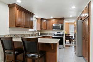 Kitchen featuring appliances with stainless steel finishes, a peninsula, a breakfast bar, light stone countertops, and recessed lighting