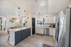 Kitchen with stainless steel appliances, white cabinets, a breakfast bar area, light wood finished floors, and vaulted ceiling