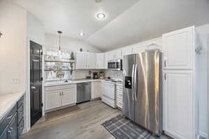 Kitchen with white cabinetry, appliances with stainless steel finishes, vaulted ceiling, light wood-style floors, and pendant lighting