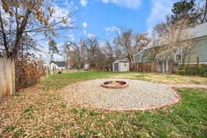 Fenced backyard featuring an outdoor fire pit and a storage unit