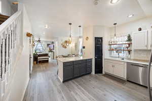Kitchen featuring a peninsula, stainless steel dishwasher, pendant lighting, tasteful backsplash, and light wood-style flooring