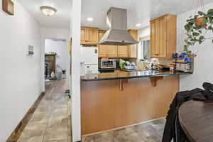 Kitchen featuring island range hood, tasteful backsplash, dark stone counters, a breakfast bar area, and freestanding refrigerator